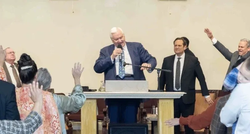 Congregation worshipping with hands raised as a minister preaches at Fortress of Truth Apostolic Church in Visalia, California
